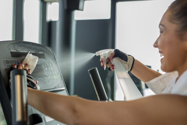 Woman cleaning gym equipment with cleaner